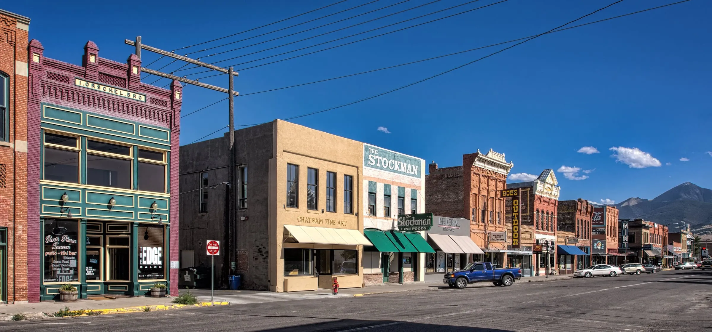 A row of historic brick and stone storefronts, including the Stockman, along a wide street with a mountain behind.